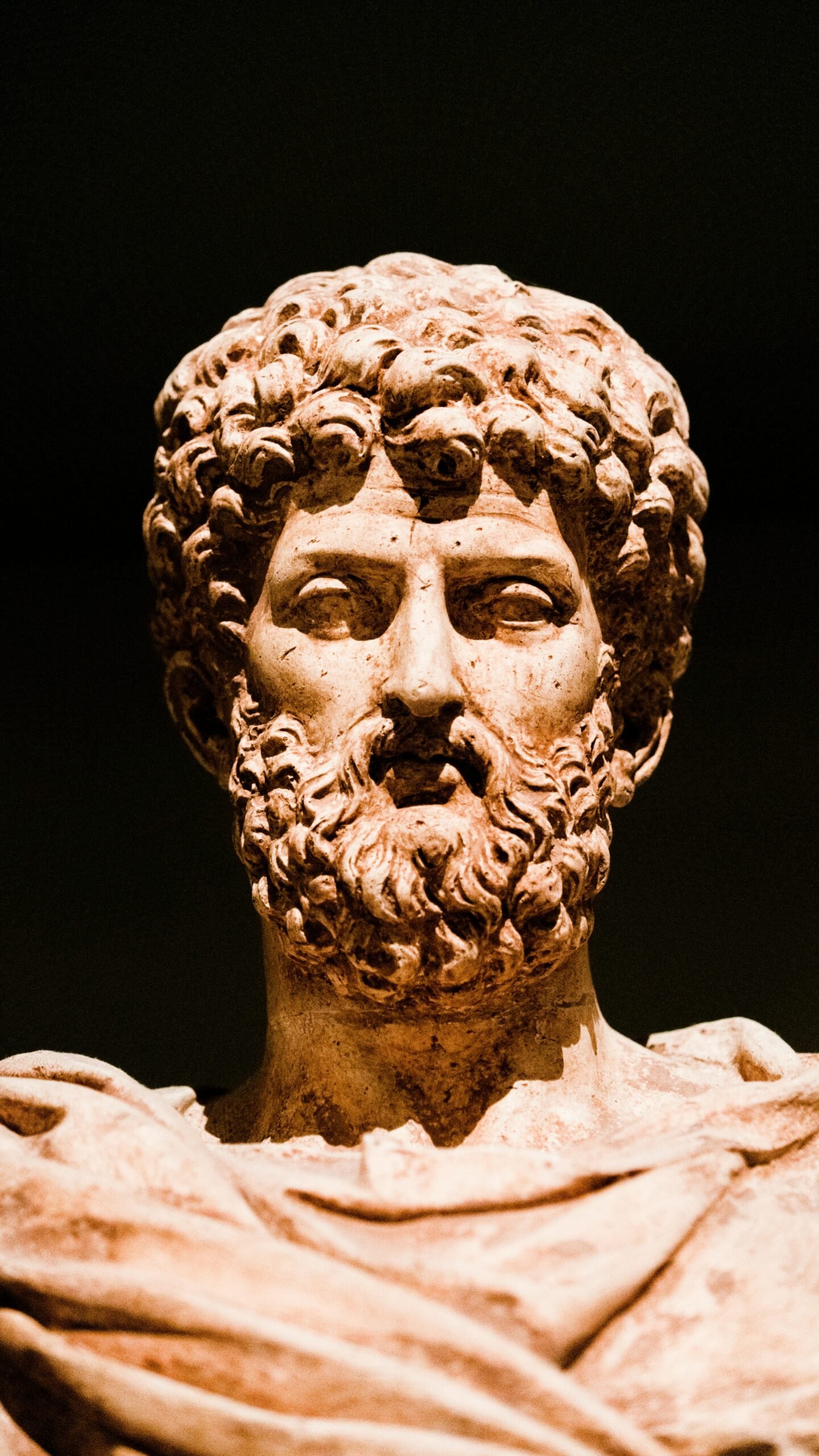 A close-up view of an ancient marble sculpture showcasing intricate facial details against a dark background.